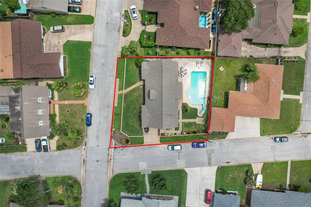This aerial photo shows a single-story home with a spacious yard, highlighted with a red border. The property features a large backyard with a swimming pool and is situated on a corner lot in a residential neighborhood. The layout includes ample driveway space and well-maintained landscaping.