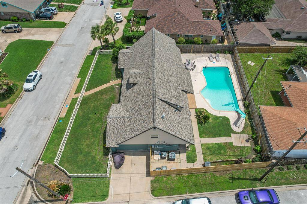 This aerial view showcases a single-story home with a spacious backyard featuring a large swimming pool and patio area. The property is fenced and located on a corner lot in a well-kept neighborhood with nearby homes.