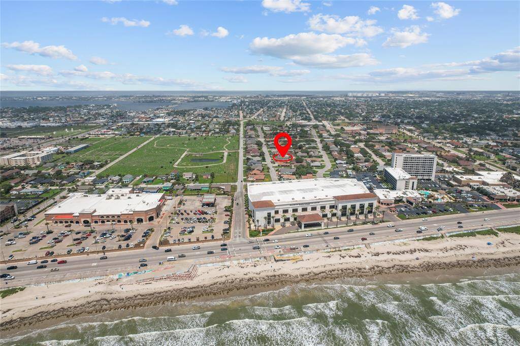 This aerial photo showcases a coastal neighborhood with a highlighted property location. It's near the beach, with convenient access to shopping areas and main roads. Ideal for those seeking a vibrant community with ocean views.
