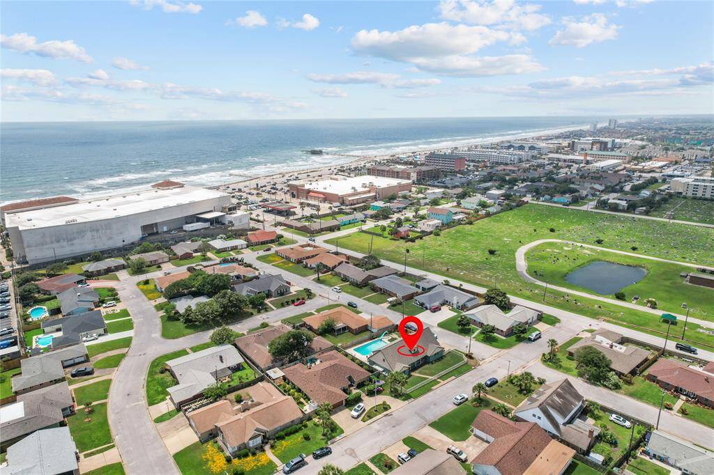 Aerial view of a coastal neighborhood featuring a home with a pool, marked for sale. It's situated near the beach, offering ocean views and close proximity to local amenities.