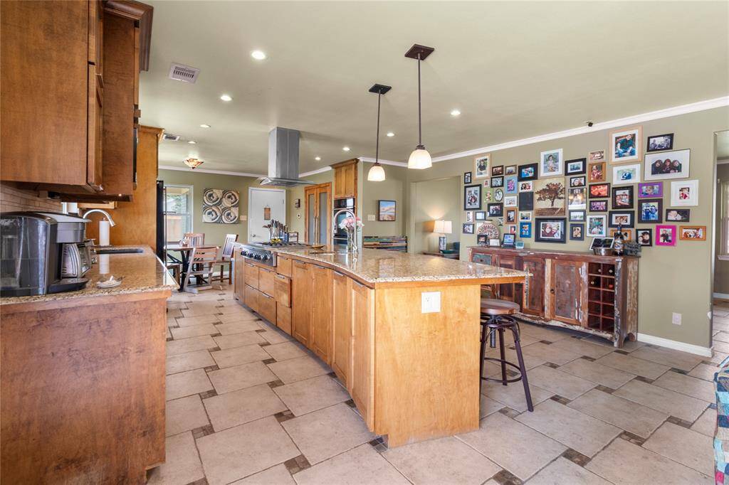 This spacious kitchen features warm wooden cabinetry, a large center island with seating, and modern stainless steel appliances. The open layout leads to a cozy dining area. The room is well-lit with recessed lighting and pendant fixtures, creating an inviting atmosphere.