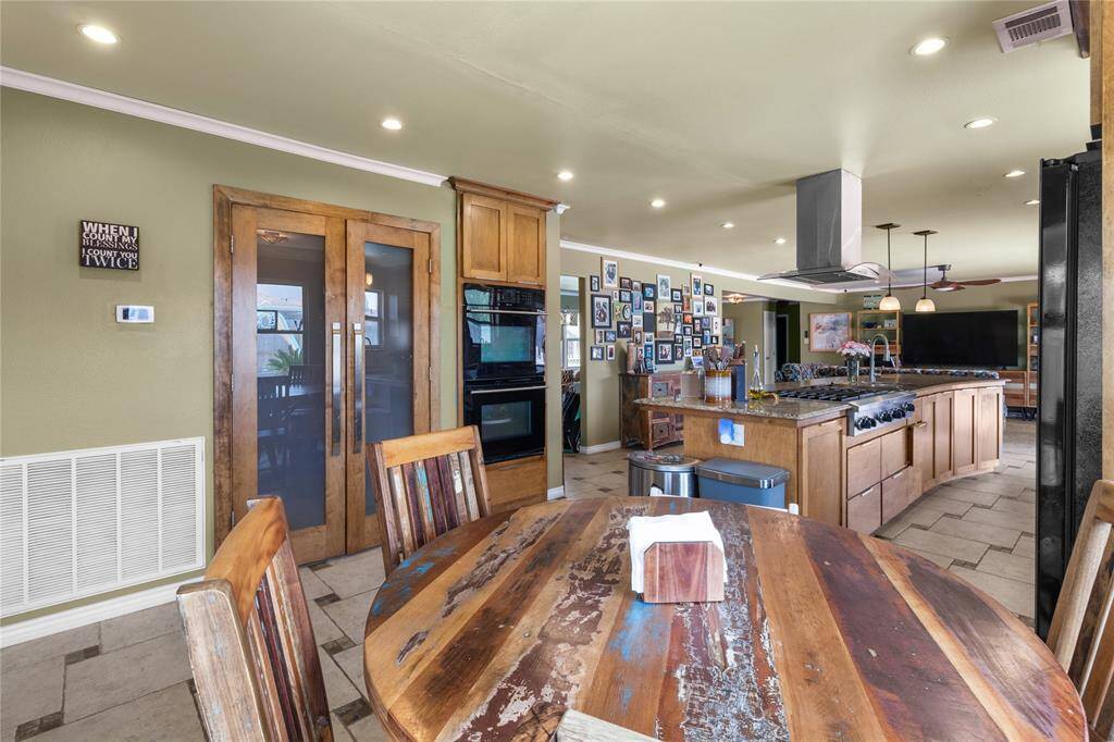 This photo showcases a spacious, open-concept kitchen and dining area. The kitchen features a large island with a gas cooktop, ample cabinetry, and modern appliances. The dining area space is well-lit with recessed lighting. A gallery wall adds a personal touch, and there is a seamless flow into the living area.