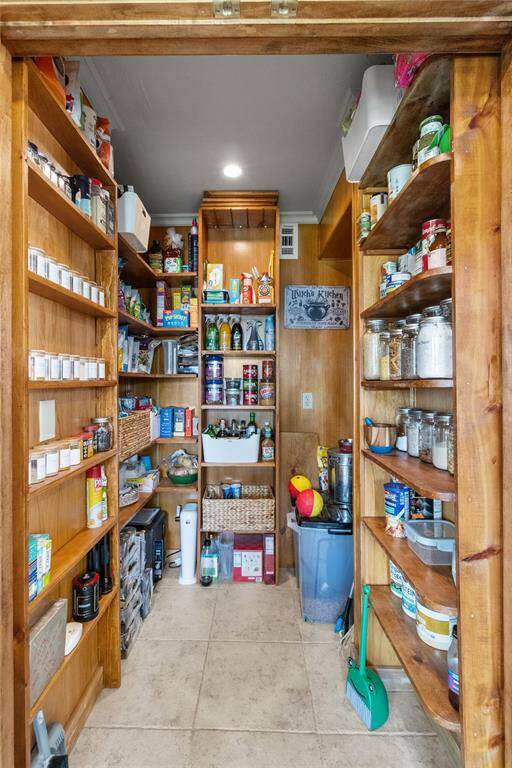 This is a spacious walk-in pantry with wooden shelves on both sides, providing ample storage for canned goods, spices, and kitchen essentials. It features a tiled floor and overhead lighting, creating a well-organized and accessible space for your kitchen needs.