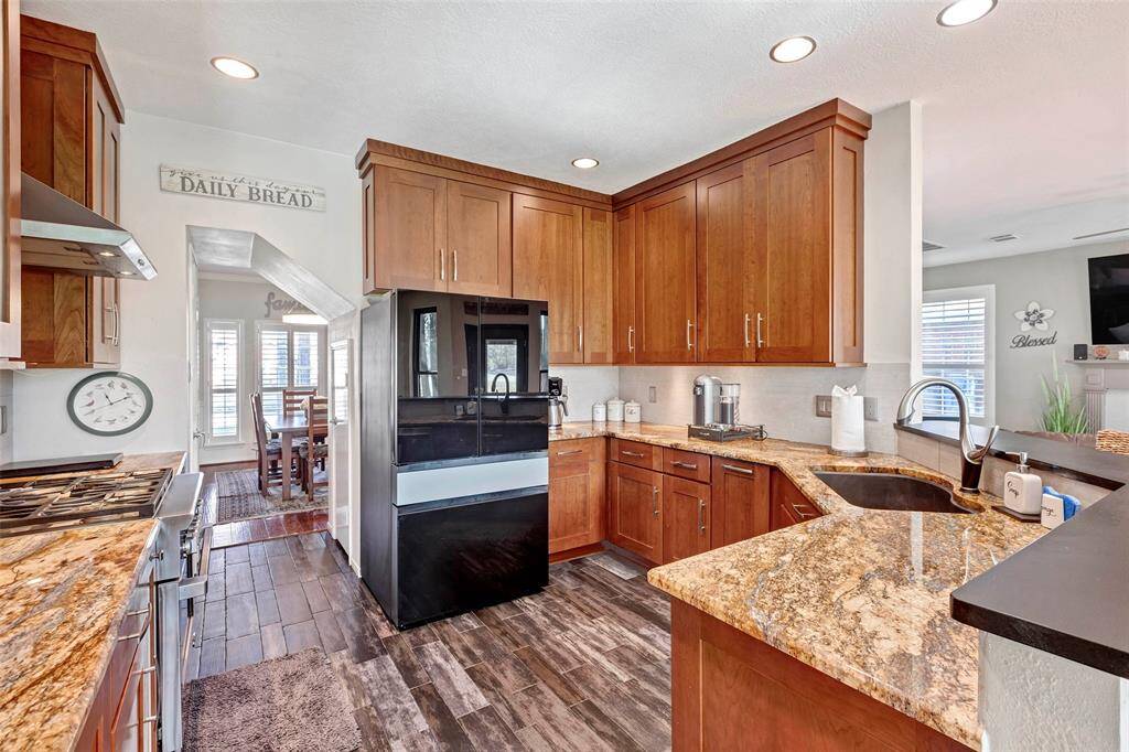This kitchen features rich wooden cabinetry, granite countertops, and modern appliances. The open layout connects to a dining area with large windows, providing ample natural light.