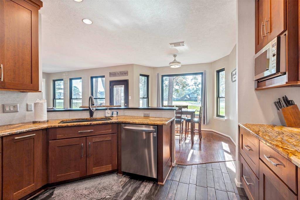 This bright kitchen features warm wooden cabinets, granite countertops, and stainless steel appliances. The open layout flows into a cozy dining area with large windows overlooking a pleasant outdoor view and golf course