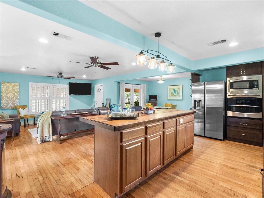 This bright, open-concept living and dining area features hardwood floors, light blue walls, and ample natural light from French doors. The space is inviting, with modern ceiling fans, cozy seating, and a stylish dining table, ideal for entertaining.