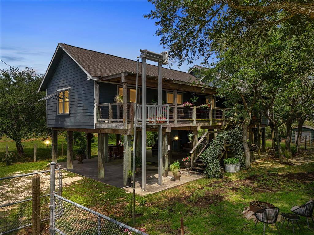 Charming elevated home with a wooden exterior, nestled among trees. Enjoy a spacious balcony, a covered area below, and a fenced yard for ultimate privacy and nature appreciation.