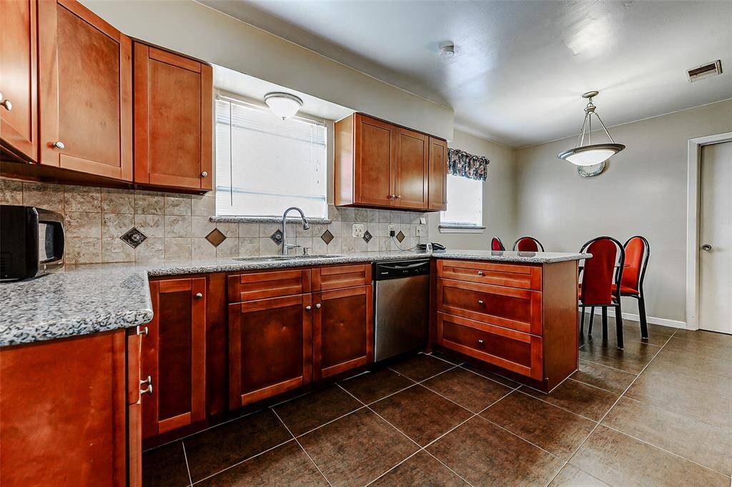 Granite countertops and tiled backsplash complement rich wood cabinetry, creating a stylish and functional kitchen space. Oversized windows above the sink allow sunlight to pour in, keeping the heart of the home light and bright.