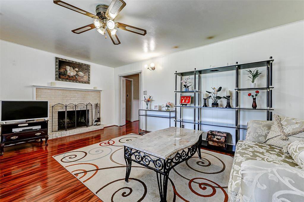 Spacious living room highlighted by a classic brick fireplace, custom shelving, and a large neutral space that’s perfect for displaying art or personal collections. Ceiling fan and hardwood floors add both comfort and style.