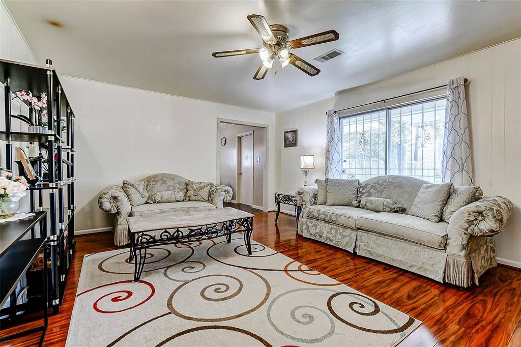 Spacious and bright living room featuring gleaming wood floors, a decorative ceiling fan, and a wall of windows bringing in natural light. This inviting space is perfect for relaxing, entertaining, and gathering with family and friends.