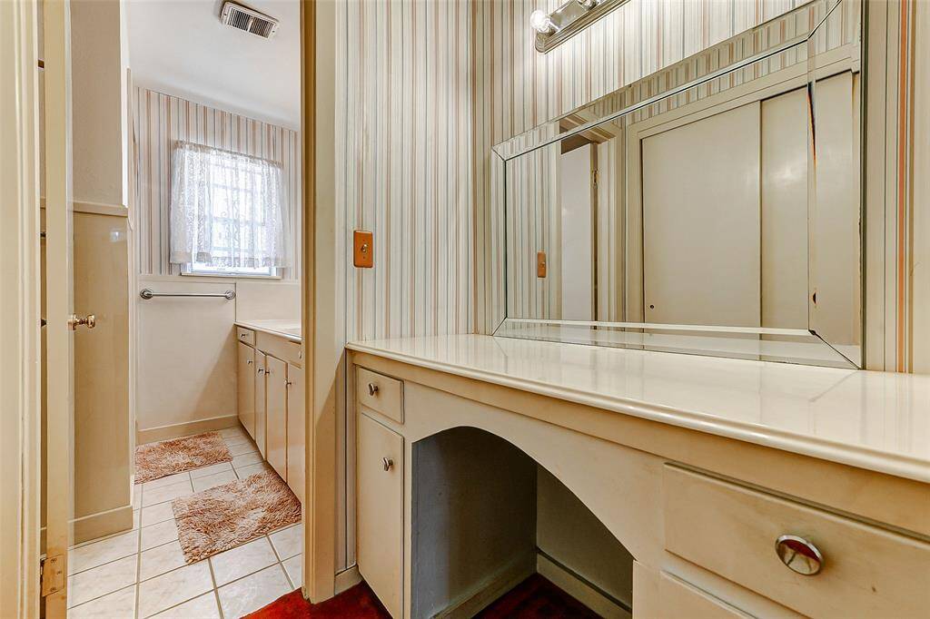 Vintage vanity space featuring charming striped wallpaper, expansive mirror, and built-in storage. This versatile area is perfect for a getting-ready nook or extra organization in the primary suite.