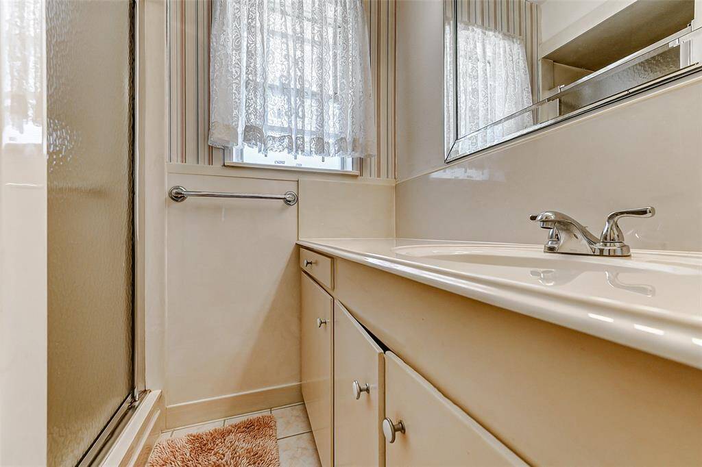 Functional and bright full bathroom featuring a standing shower, tile floors, and a long vanity for extra storage. A frosted window brings in natural light while maintaining privacy. Ready for your personal updates!