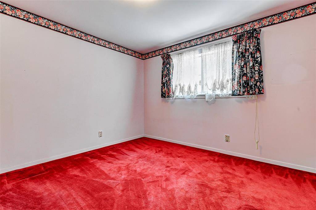 Bright secondary bedroom with vibrant red carpeting, floral accent border, and a large window letting in beautiful natural light. Perfect as a guest room, creative space, or a charming child's bedroom ready for a new vision.