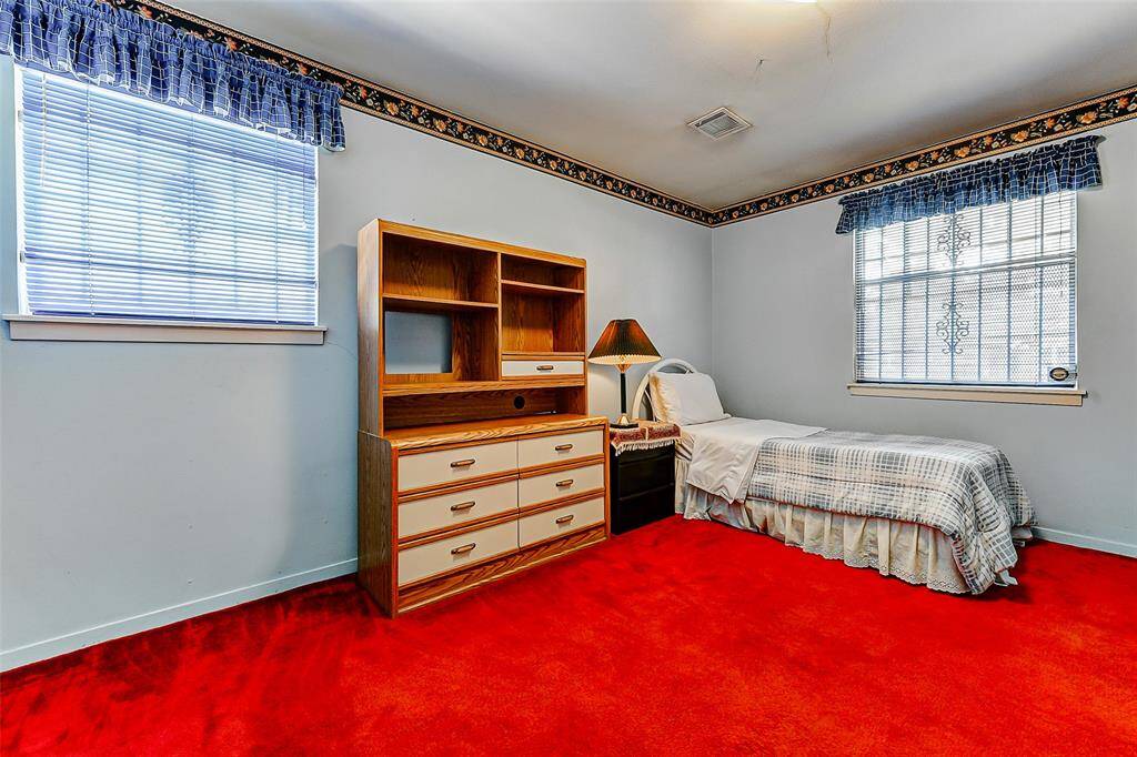 Generously sized secondary bedroom boasting a work-from-home setup with a cozy desk area. The colorful carpet and classic finishes provide a playful backdrop for creative possibilities.