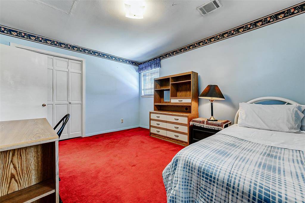 Bright and welcoming secondary bedroom featuring a large window that lets in plenty of natural light. Classic details include a charming floral border and bold red carpet. The cozy layout offers both comfort and function for family or guests.