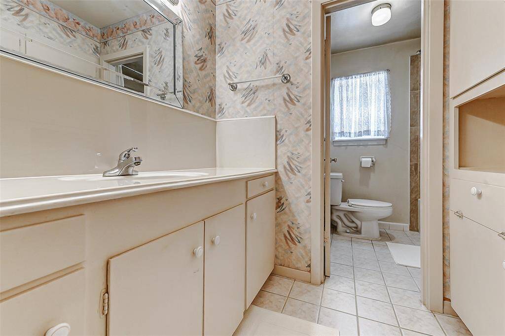 Updated secondary bathroom with neutral tile flooring, expansive vanity with storage, and stylish wallpaper accents. The perfect setup for a shared bath offering functionality and charm.