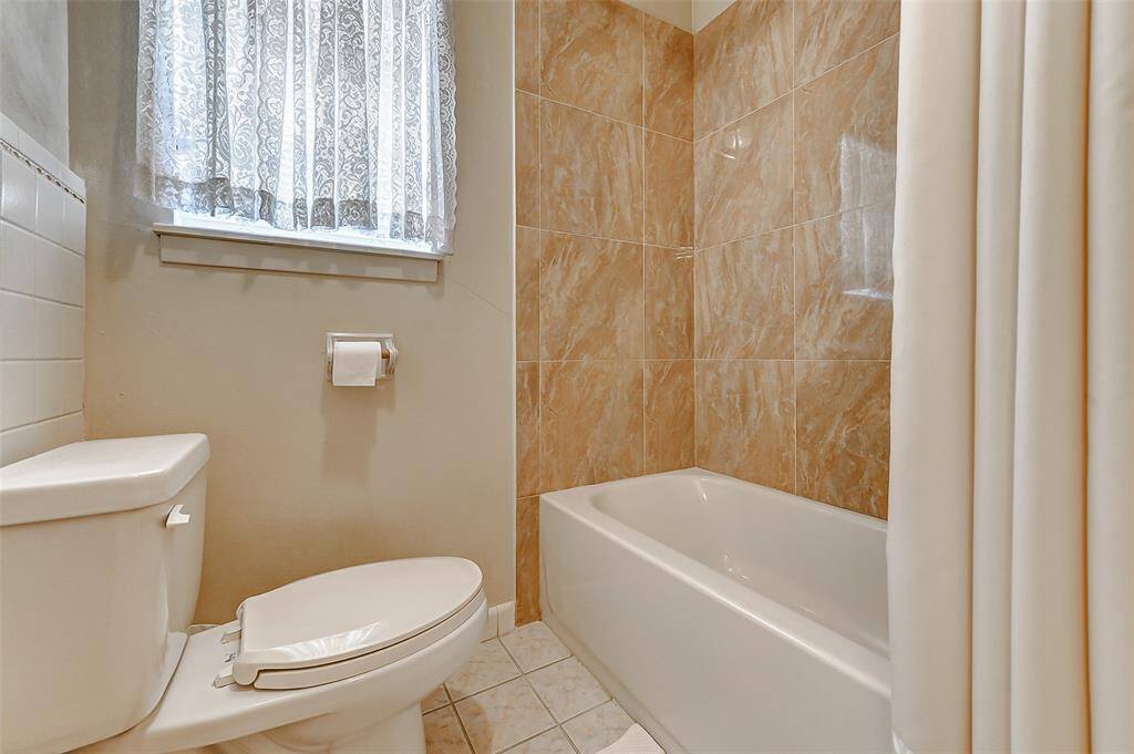 Fresh and bright bathroom featuring a fully tiled tub and shower combo, updated tile work, and a large window for soft, natural light. Ready for daily routines with style and ease.
