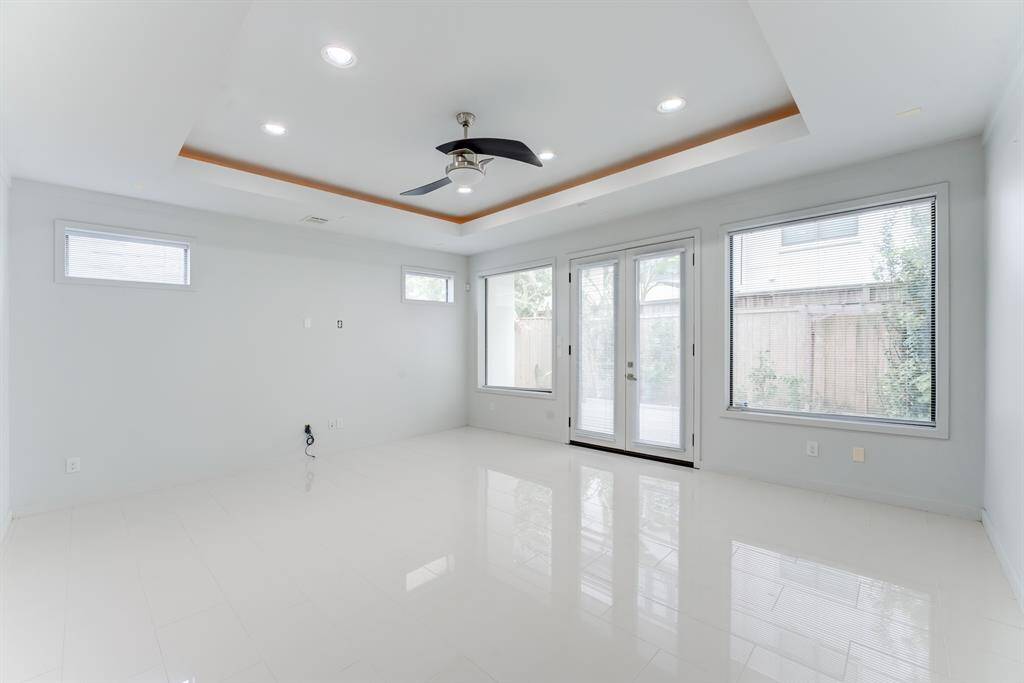Bright and spacious living room with large windows, recessed lighting, and a ceiling fan. The neutral walls and glossy tile flooring enhance the open feel, while glass doors provide outdoor access.