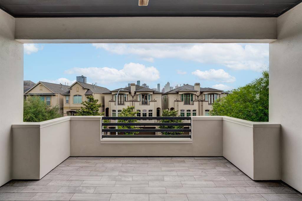 Spacious balcony with modern railing and tile flooring, offering a view of neighboring homes and the city skyline in the distance. Perfect for outdoor relaxation and enjoying the scenery.