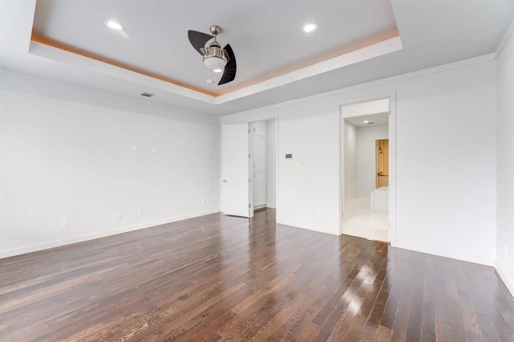 This principal bedroom features polished hardwood floors, recessed lighting, and a modern ceiling fan. It has a tray ceiling with accent lighting and en suite bathroom.