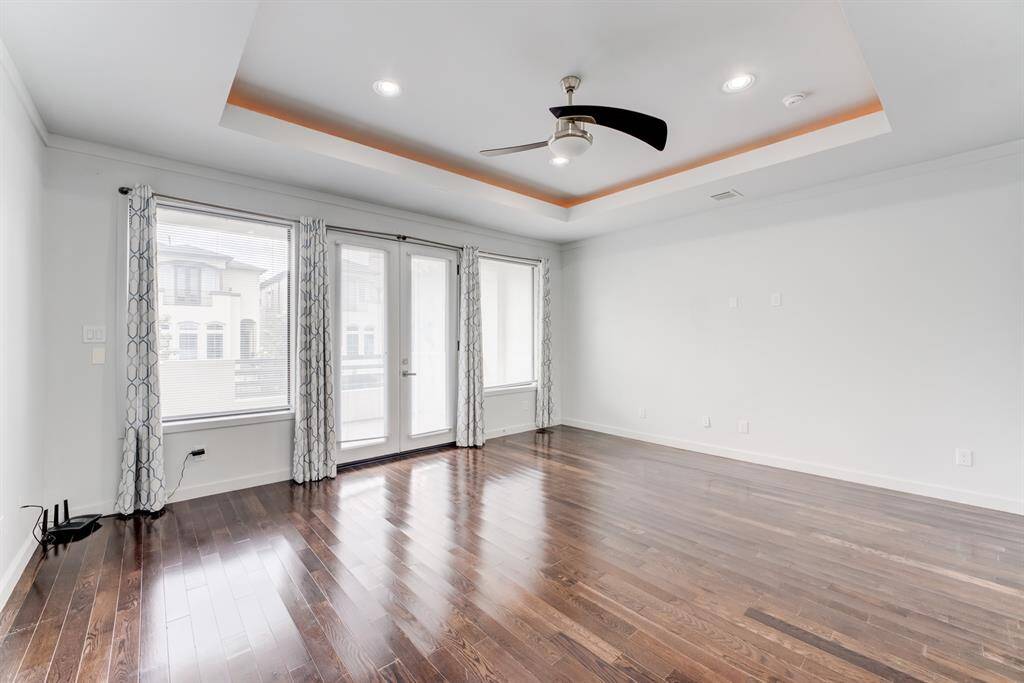 Spacious Principal bedroom with hardwood floors, large windows, and modern ceiling fan. Features a tray ceiling with recessed lighting and access to a balcony.