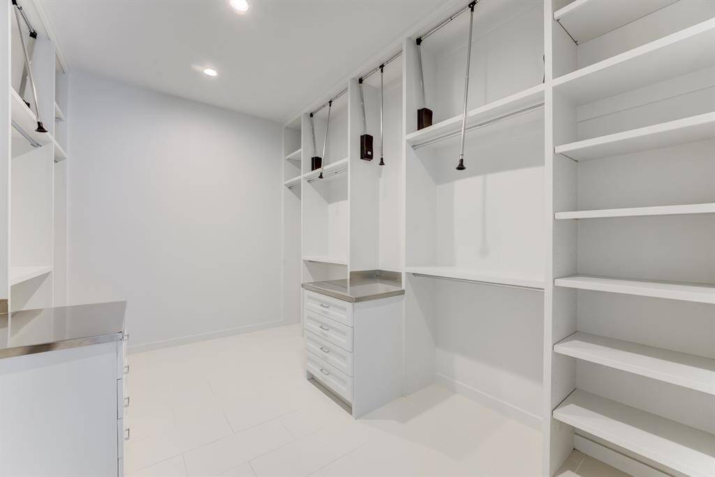 Spacious walk-in closet with ample shelving and drawer space, featuring pull-down rods for convenience. Bright, modern design with recessed lighting and sleek finishes.