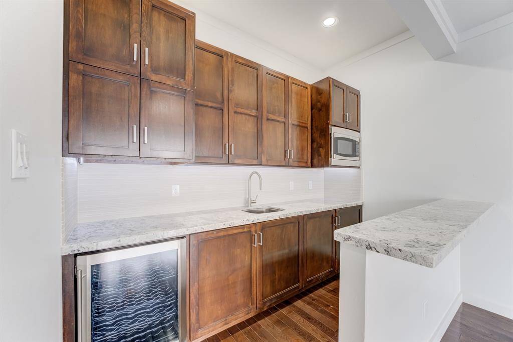 This kitchen features elegant wooden cabinetry, a sleek granite countertop, a built-in microwave, and a wine cooler. The bright and airy space is perfect for cooking and entertaining.
