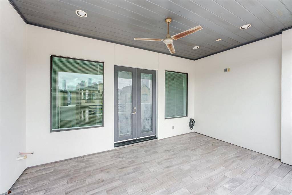 This photo showcases a spacious, covered patio with modern tile flooring and a ceiling fan. It features large windows and double doors, offering plenty of natural light and a view of the surrounding area, ideal for relaxing or entertaining.