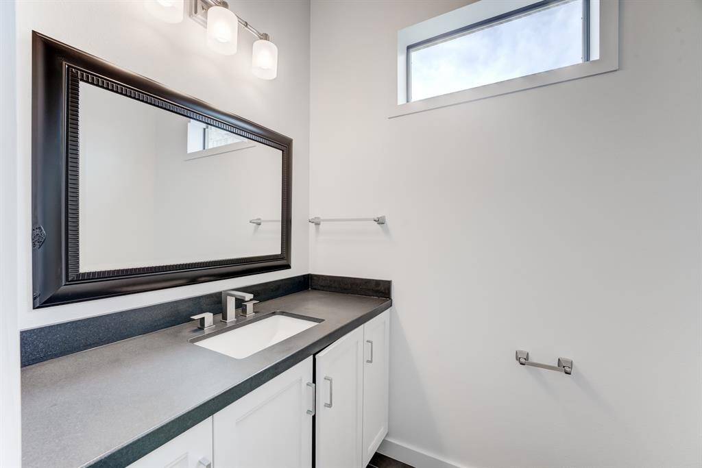 This bathroom features a modern design with a large framed mirror, sleek single-sink vanity with a dark countertop, and a rectangular window providing natural light.