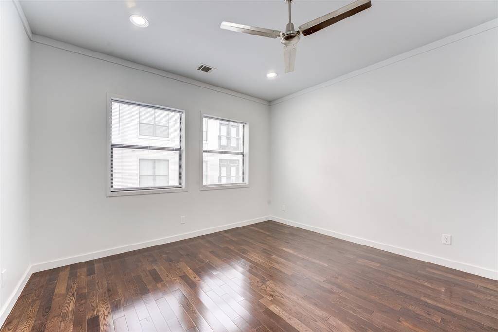 Bright, spacious room with hardwood floors, two large windows for natural light, recessed lighting, and a modern ceiling fan. Ideal for a bedroom or office space.