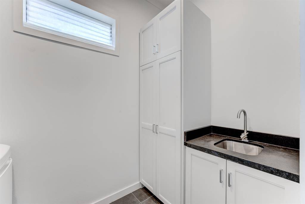 Compact and modern laundry room with a sleek sink, ample cabinet storage, and a bright window, perfect for efficient organization.