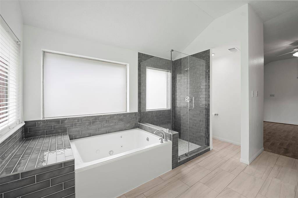 Primary bathroom has a spa like feel with its jetted tub, oversized custom frameless shower, and subway tile.