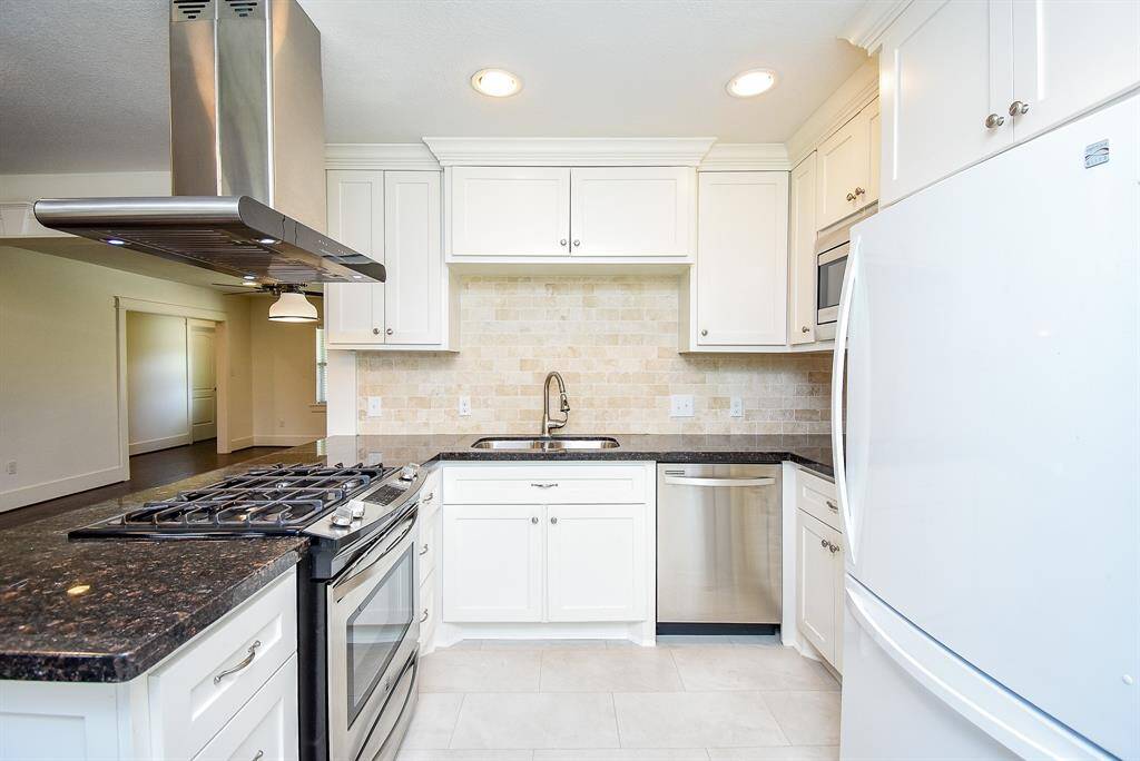 Spacious kitchen featuring granite countertops and a stylish tile backsplash.