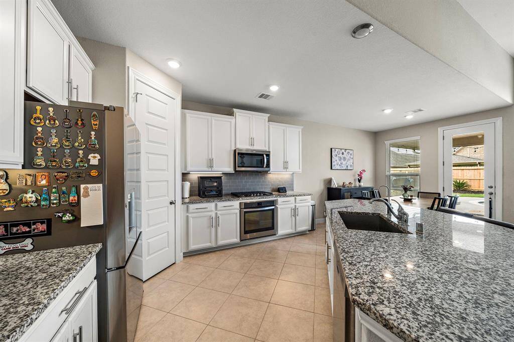 This modern kitchen features crisp white cabinetry, granite countertops, and a stylish subway tile backsplash for a clean, polished look. The spacious layout connects effortlessly to the dining area and backyard, perfect for everyday meals or entertaining guests.