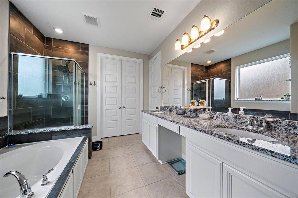 Step into the luxurious primary bath boasting dual vanities with granite countertops, a large soaking tub, and an oversized walk-in shower. Thoughtful details like upgraded tilework and abundant storage enhance both style and functionality.