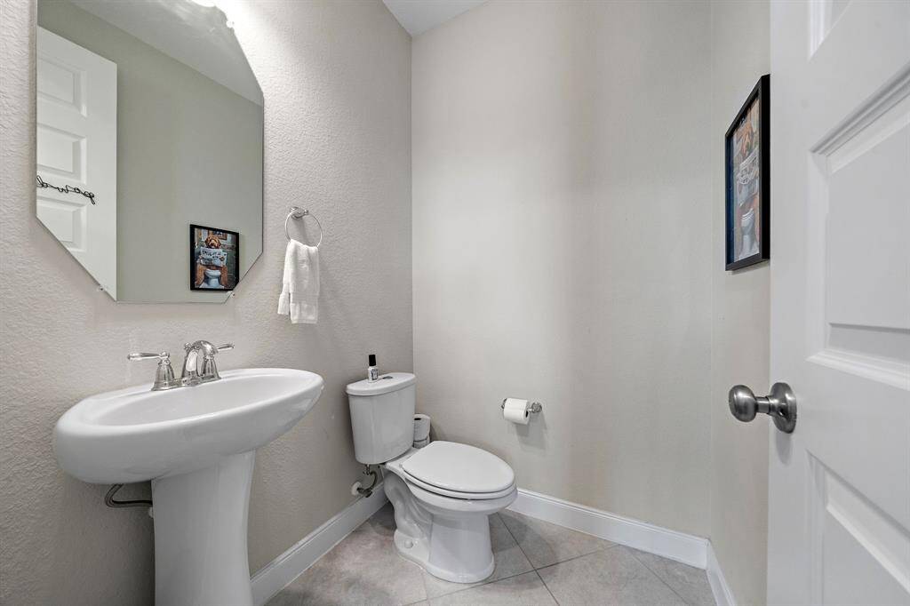 The downstairs powder bath features a sleek pedestal sink and modern fixtures, providing a polished space for guests. Neutral tones and a simple, functional layout make it a stylish and convenient addition to the main floor.