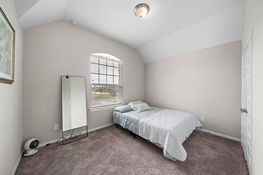 This light-filled bedroom features a charming arched window and vaulted ceiling, adding character and dimension to the space. Plush carpeting and a neutral palette make it easy to personalize.