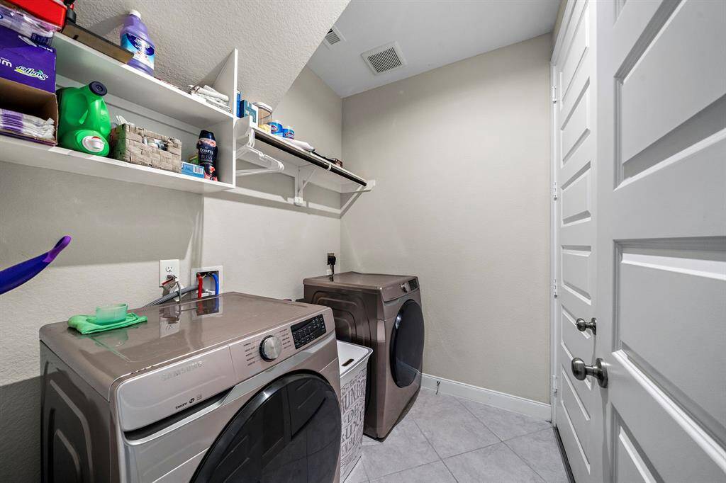 The spacious laundry room offers built-in shelving and a hanging rod for easy organization. With tile flooring and convenient access to the garage, it’s designed to keep household tasks efficient and out of sight.