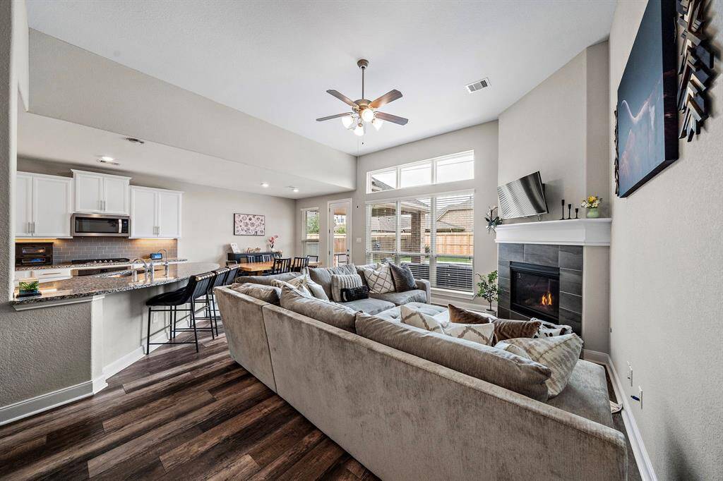 This inviting living room offers a seamless open-concept layout that flows effortlessly into the kitchen and dining areas, making it perfect for both entertaining and everyday living. A gas fireplace serves as a cozy focal point, while large windows overlook the backyard oasis and let in soft natural light.