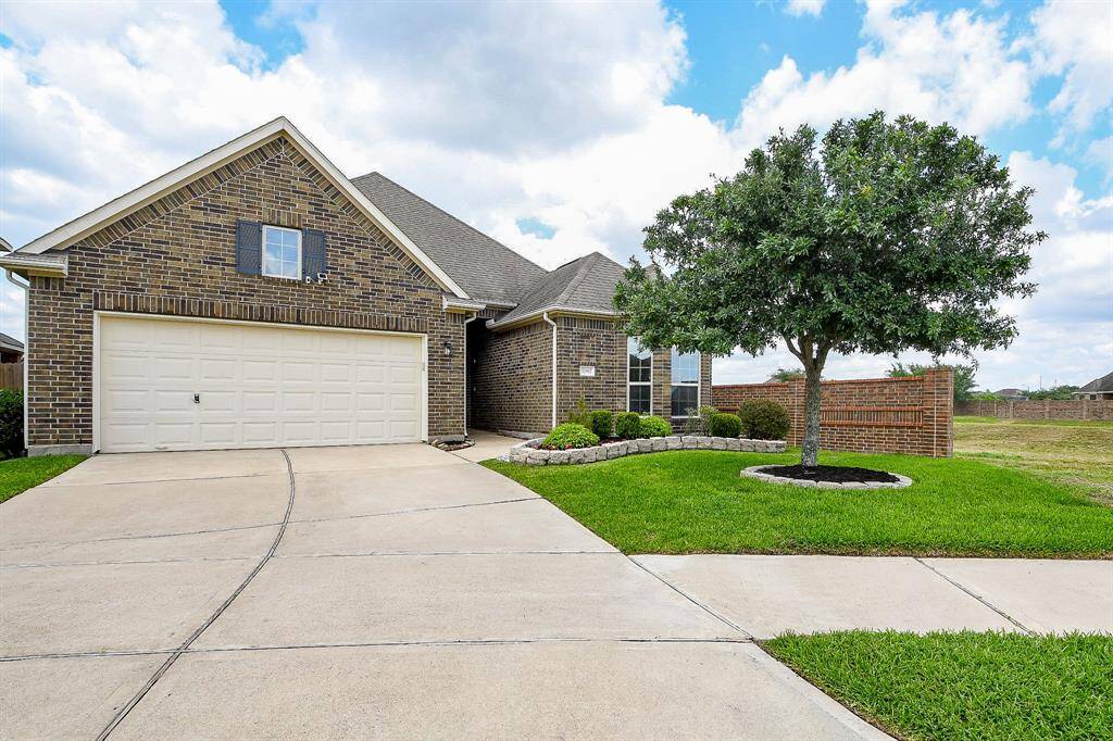 A charming single-story brick home with a two-car garage. The property has a well-maintained front yard with a neatly trimmed lawn and a mature tree, offering excellent curb appeal.