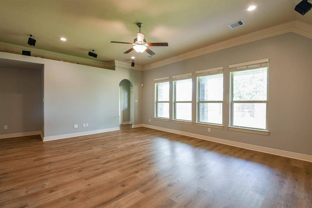 This spacious living room features new vinyl floors, abundant natural light from multiple windows, and a ceiling fan. The neutral wall color and recessed lighting create a warm, inviting atmosphere.