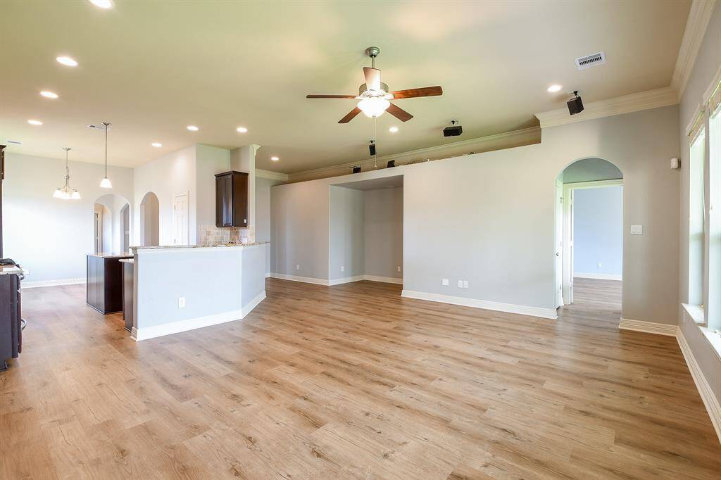 This spacious open-concept living area features new light LVP flooring, neutral walls, and plenty of recessed lighting. It includes a ceiling fan, large windows for natural light, and an adjacent kitchen with modern fixtures and an arched doorway leading to additional rooms.