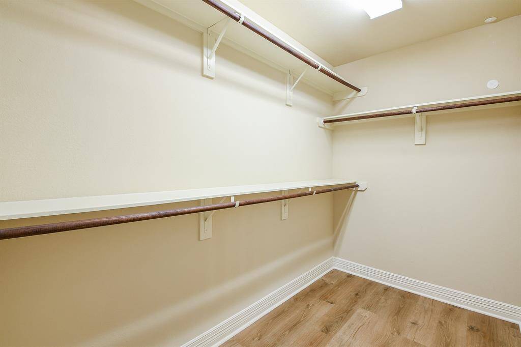 Spacious walk-in closet with ample shelving and hanging space, featuring light wood flooring and neutral walls for a bright, organized feel.