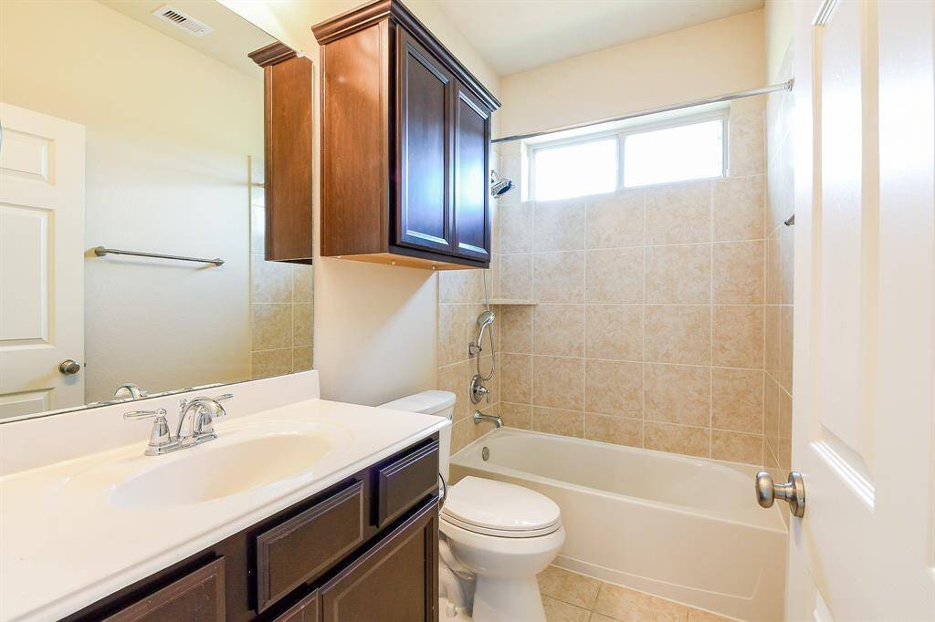 Another secondary bathroom features a clean, modern design with a tile-surround bathtub, a white vanity with a sleek faucet, and dark wood cabinetry for storage. A window above the tub provides natural light.