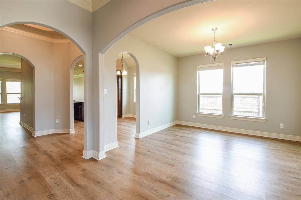 A bright, open-concept living space with light wood flooring and soft gray walls. It features elegant archways and large windows that allow natural light to fill the room, creating an inviting atmosphere.