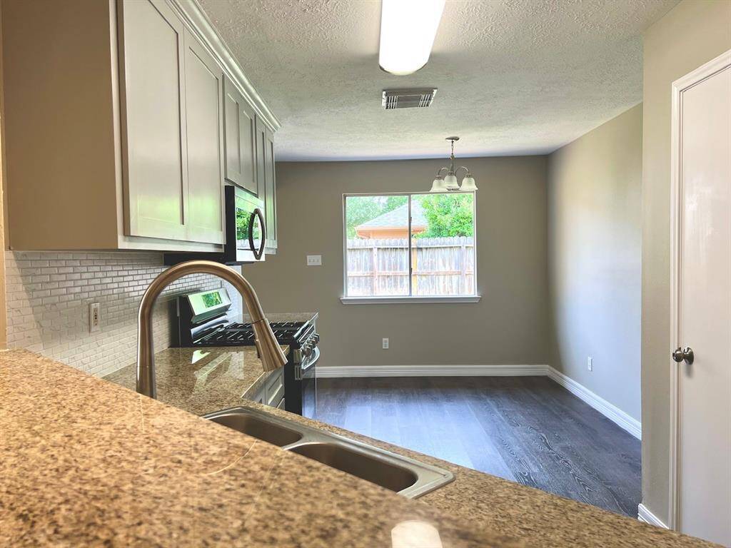 Bright and modern kitchen with granite countertops, stainless steel sink, and a tiled backsplash. It features ample cabinetry, a gas stove, and a dining area with a large window offering natural light.