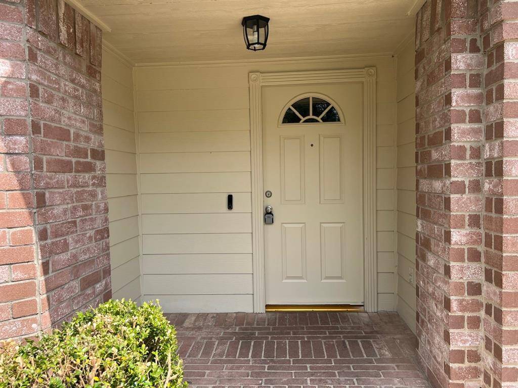 A welcoming front entrance with a neatly painted door, framed by brickwork and siding. It features a modern light fixture and a small garden area, creating a cozy and inviting first impression.