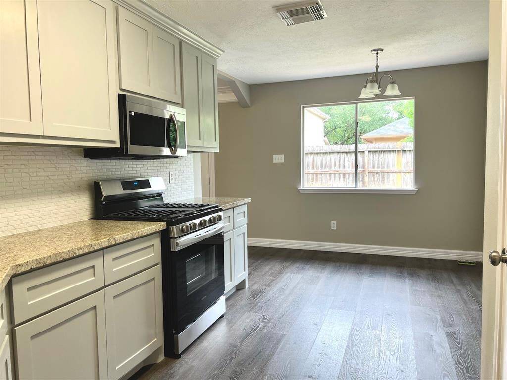 Bright kitchen with modern appliances, spacious countertops, and sleek cabinetry. It features a large window for natural light and wood-style flooring, creating a warm and inviting space.