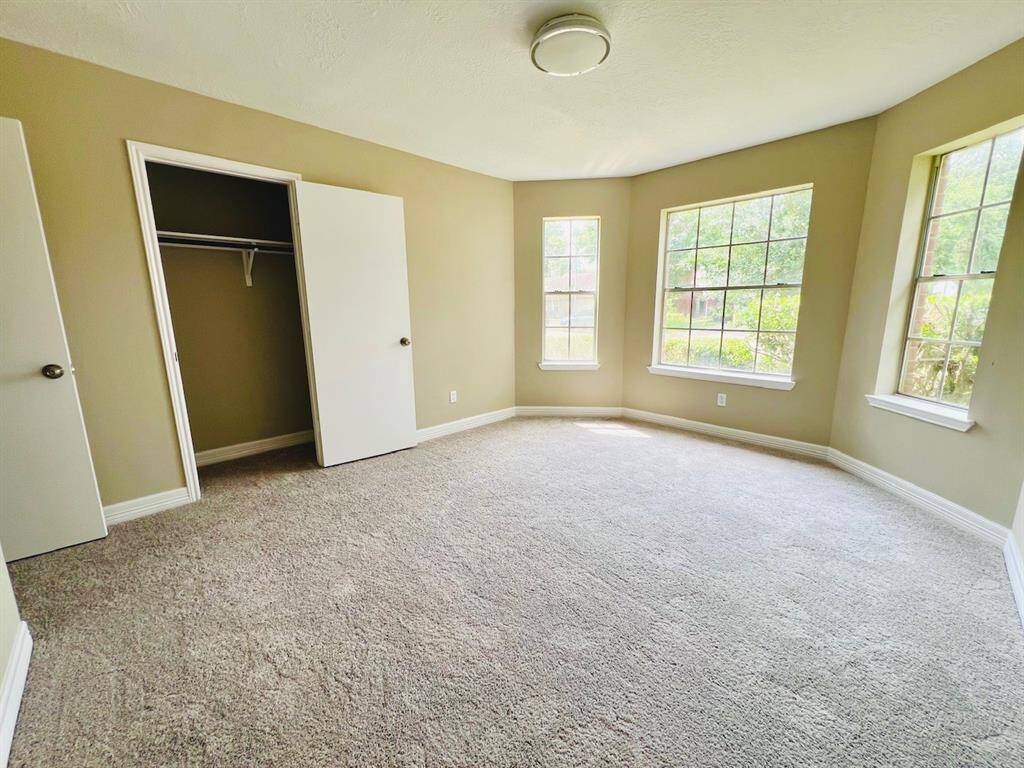 Bright, spacious bedroom with neutral walls and carpet, featuring large windows for natural light and a closet for storage.