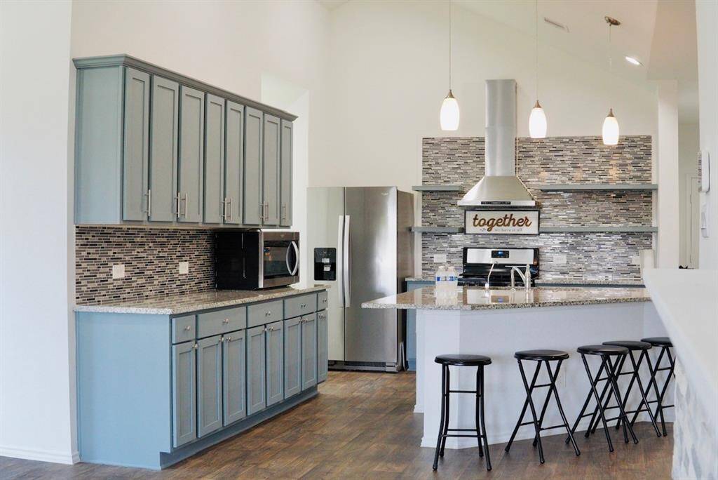 Kitchen with granite countertop, wood cabinet, upgraded range hood fan and floating shelves.